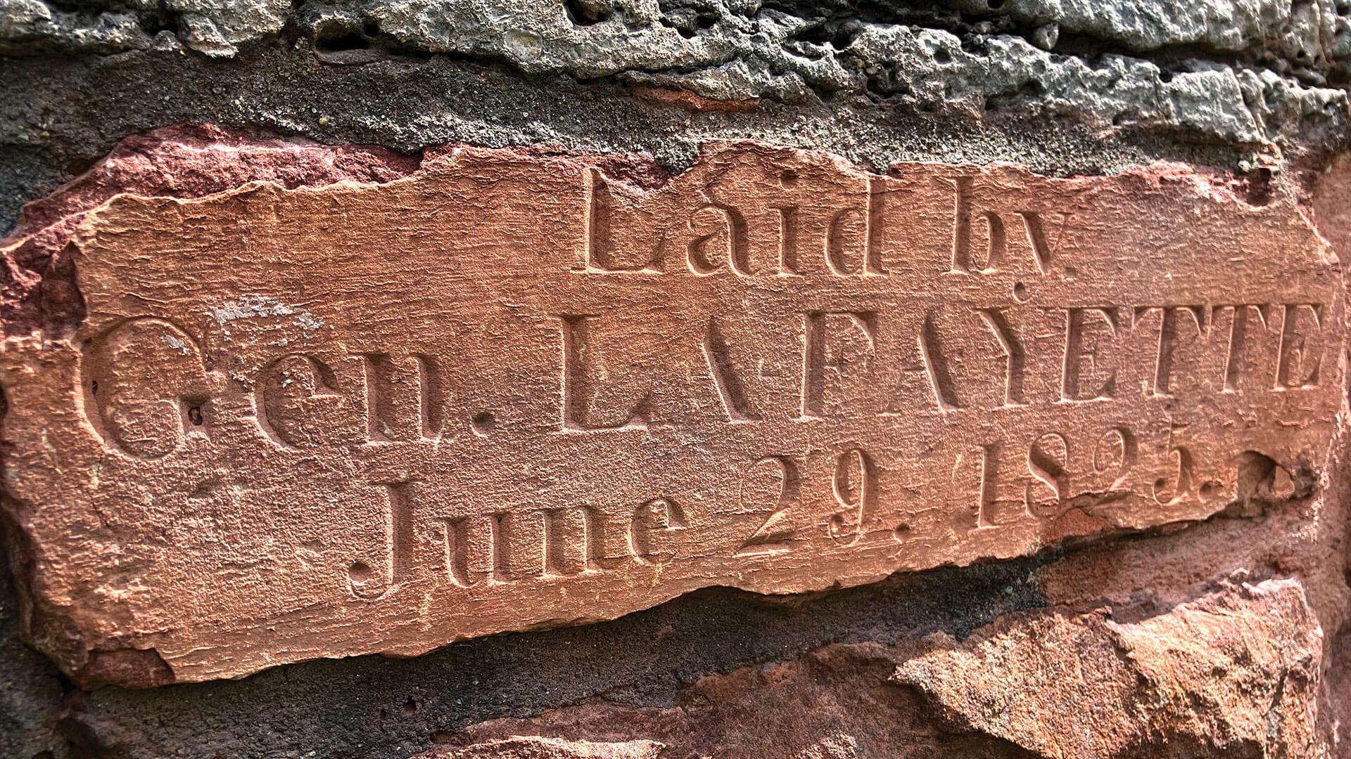 close up of a brick stone with the text laid by Gen. Lafayette june 29 1825 engraved into it