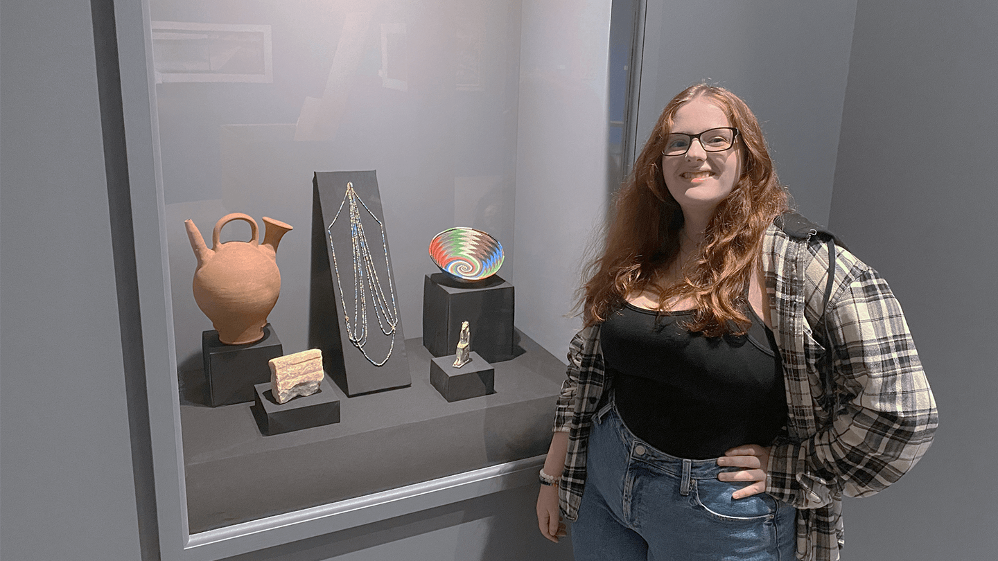 UVM student Tura Furrow-Scott stands next to display of cultural works at the Fleming Museum.