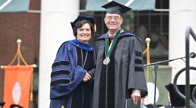man in regalia receiving diploma from woman