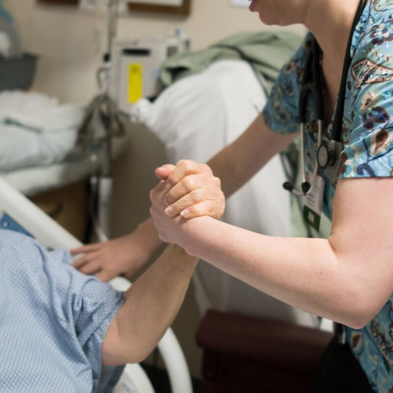 clinicians and patient in hospital bed grasping hands