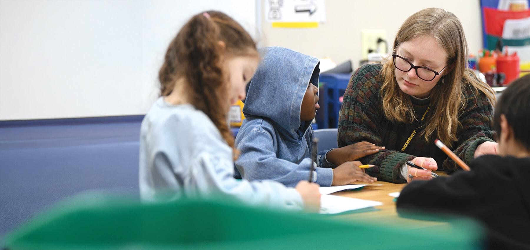 a student works at a desk intently with children in a classroom