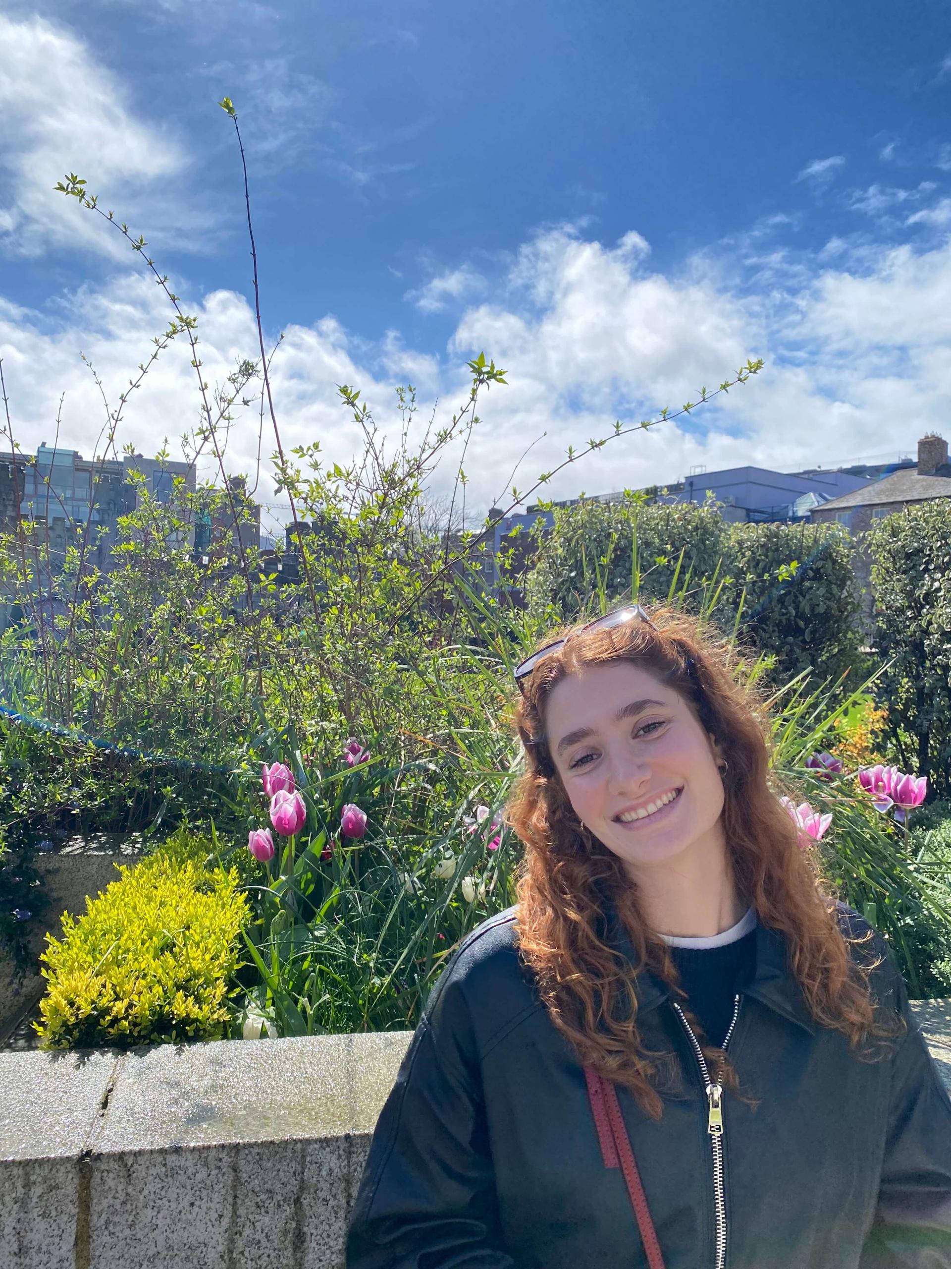Chloe, outdoors, in front of a blooming garden.
