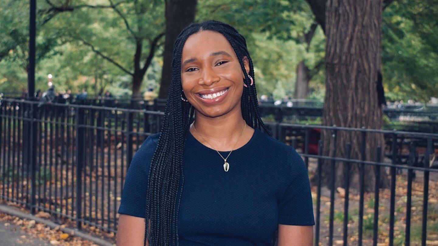 a person smiling at the camera in front of a fence