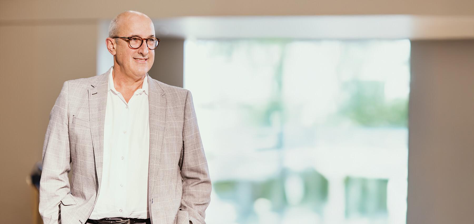 a man with glasses standing against a window
