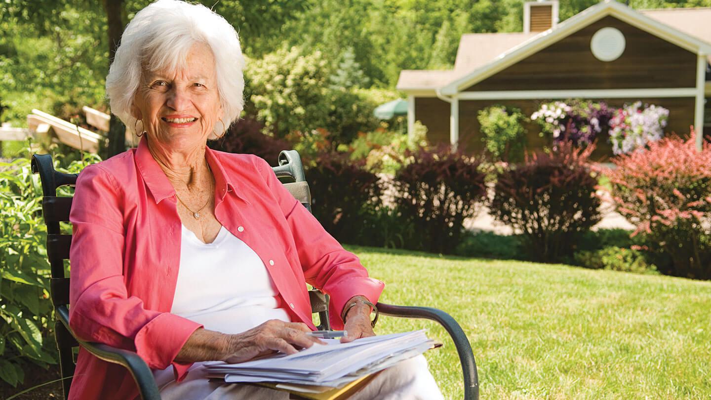 woman sitting in a chair surrounded by a house and green lawn