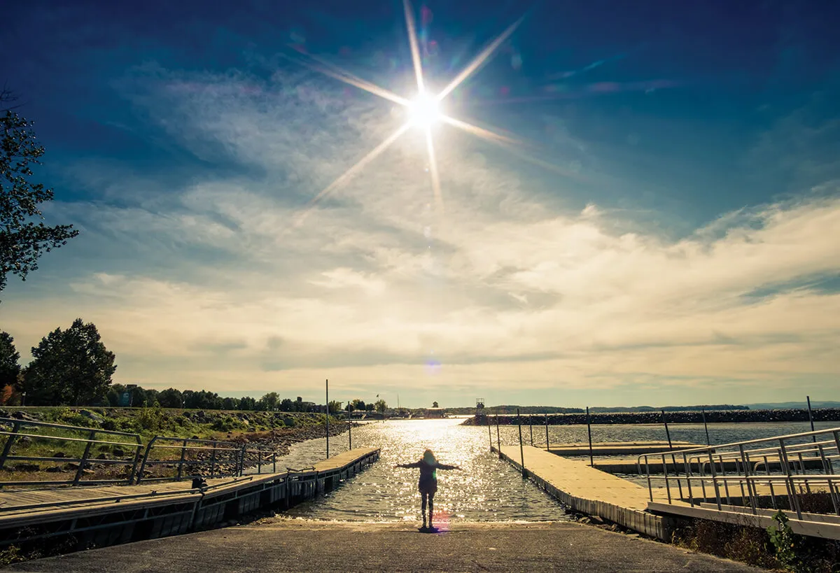 Person standing at Lake with winter sun in sky