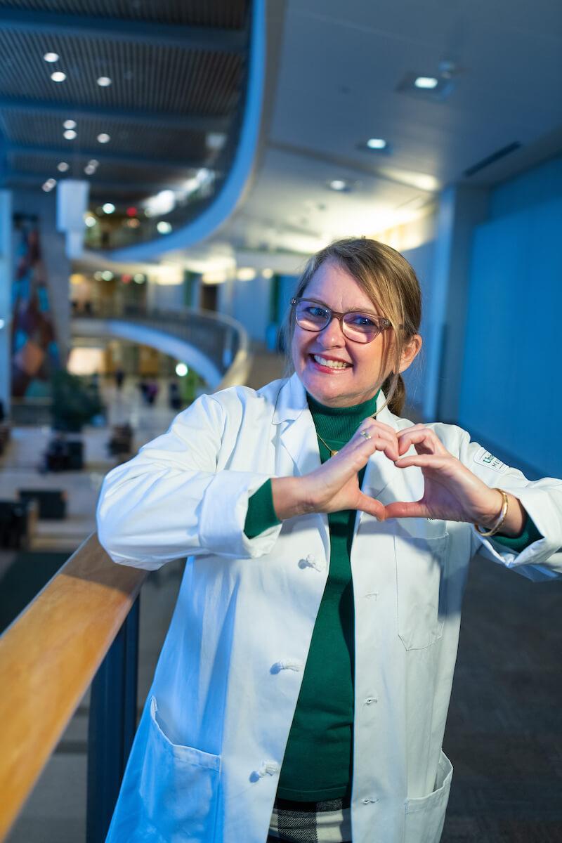 Person smiling in a hallway making a heart with their hands