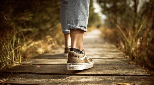 view of person's ankles and sneakers while walking on boardwalk in woods