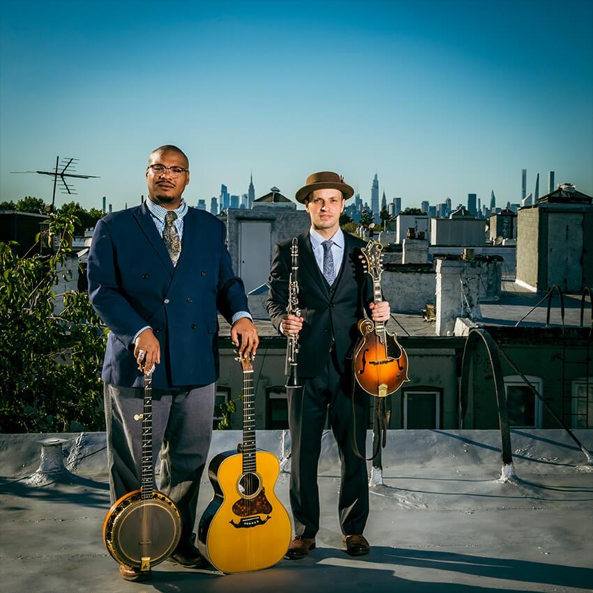 Jerron Paxton holding a banjo and a guitar and Dennis Lichtman holding a clarinet and a mandolin.