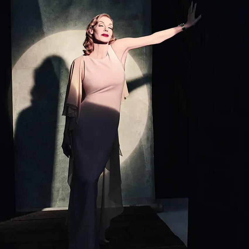 Ute Lemper standing in a spotlight wearing a pale pink dress