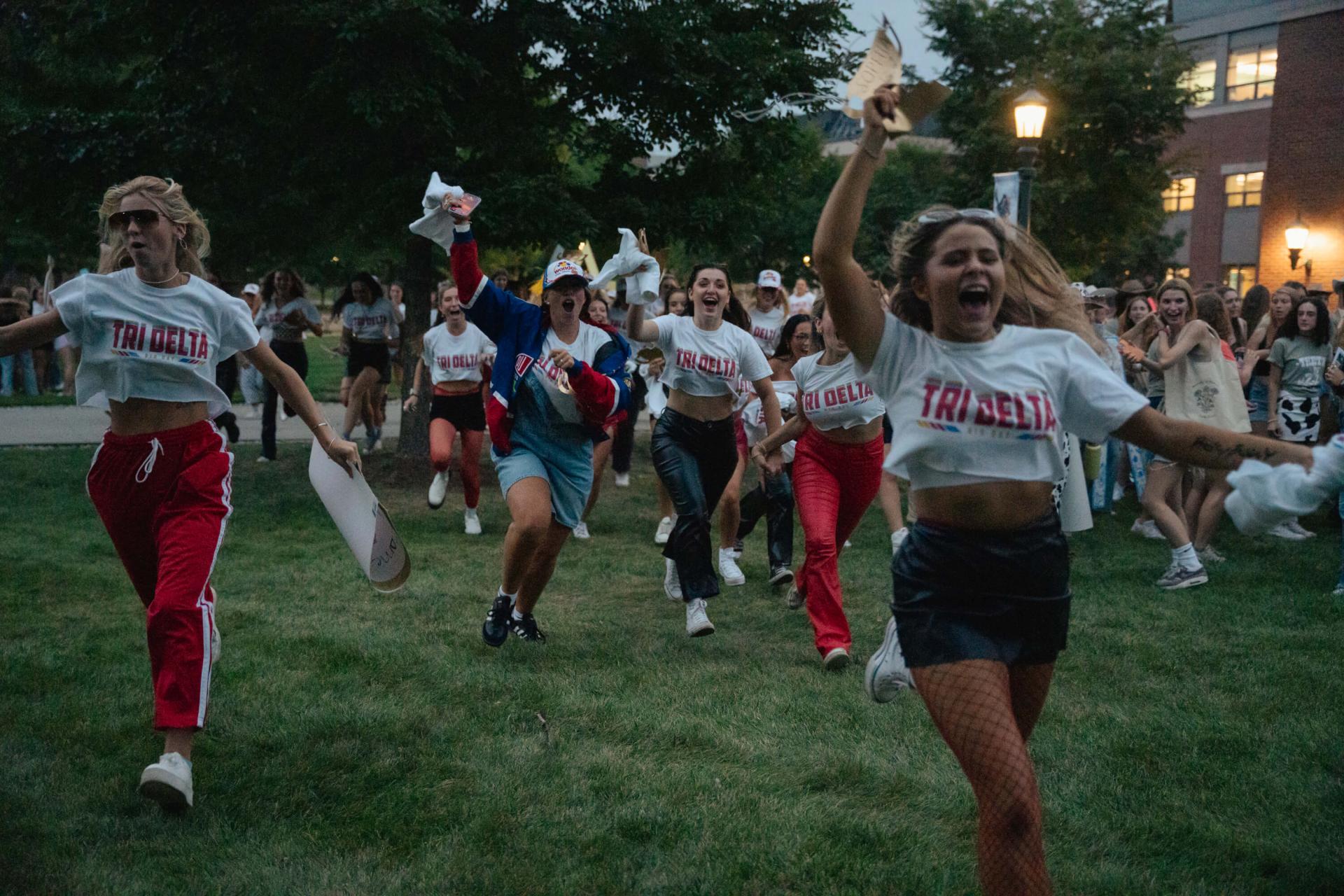 A group of sorority women run across the Davis Center green on bid day