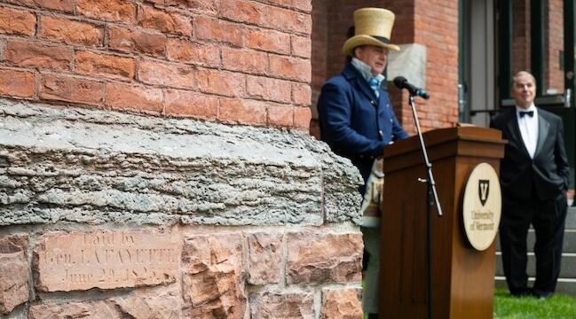 A Lafayette interpreter speaks at the event. In the foreground is the original cornerstone of Old Mill that was laid by General Lafayette in 1825.