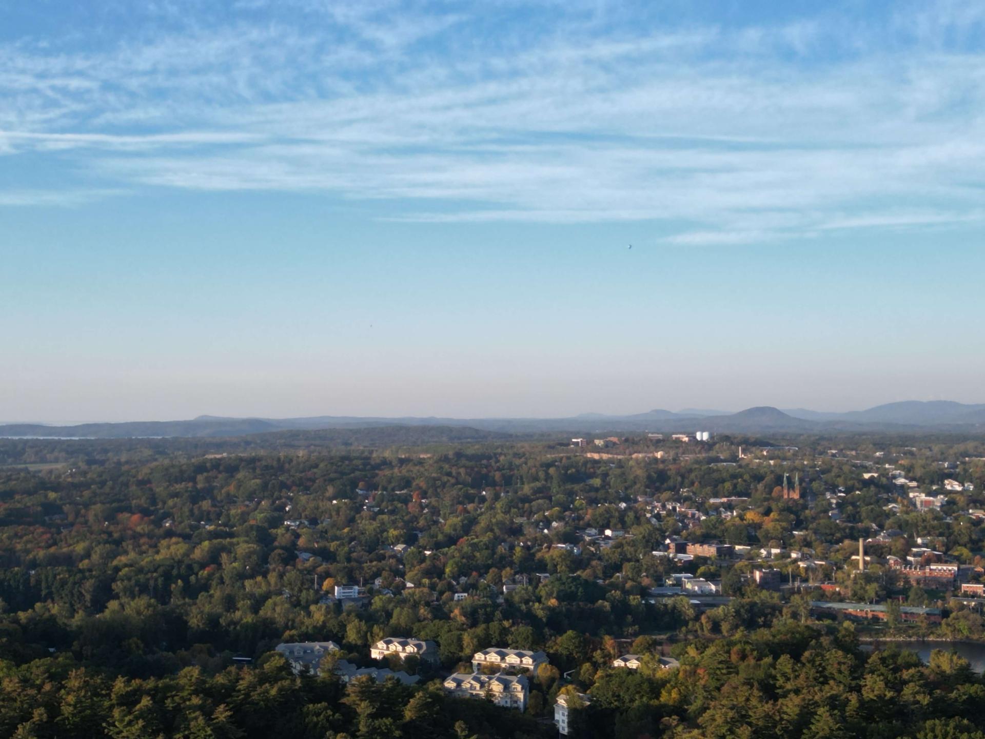 Aerial view of a town with trees, the sky and mountain range in the distance.
