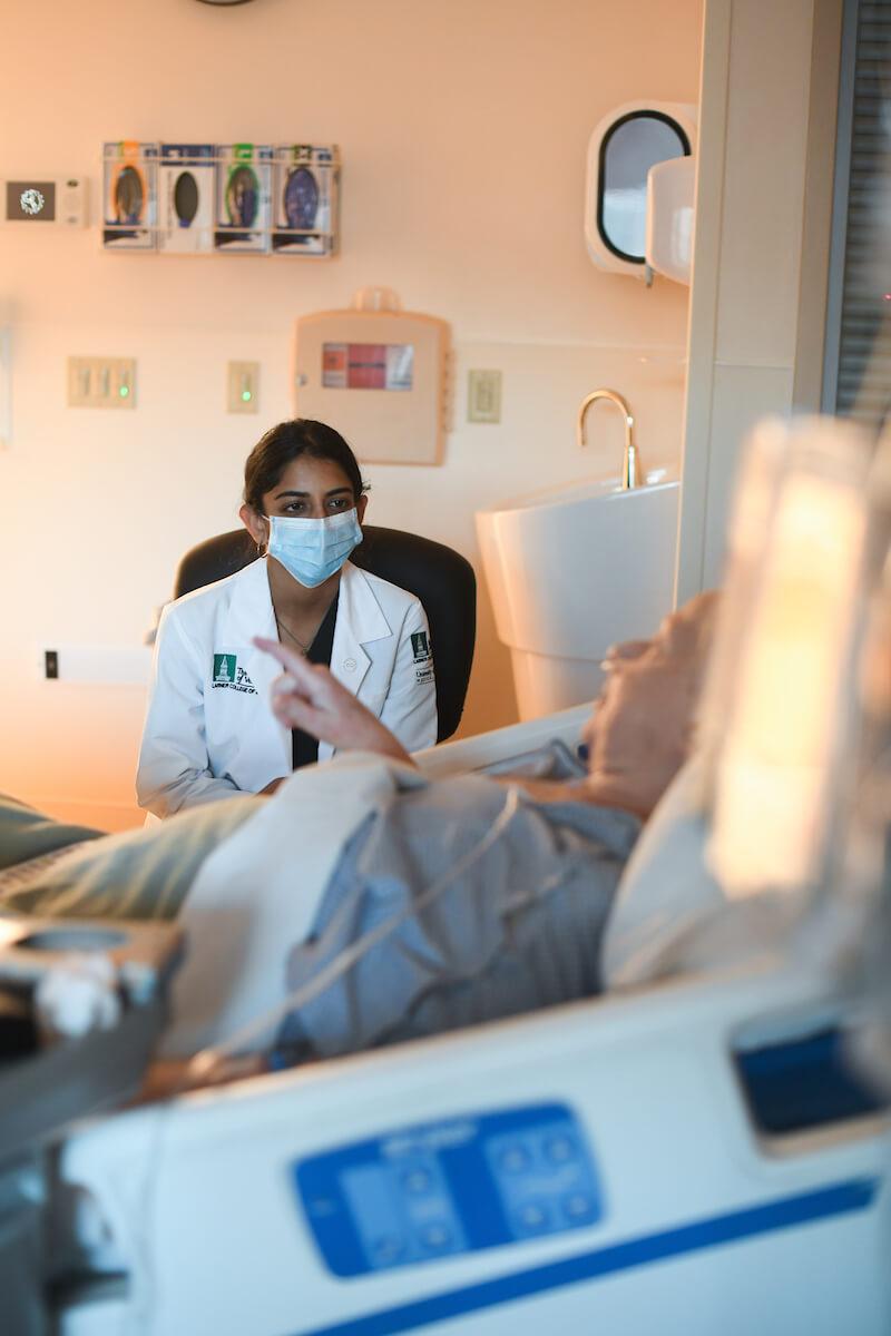 Doctor with a mask on sitting by patient's bedside