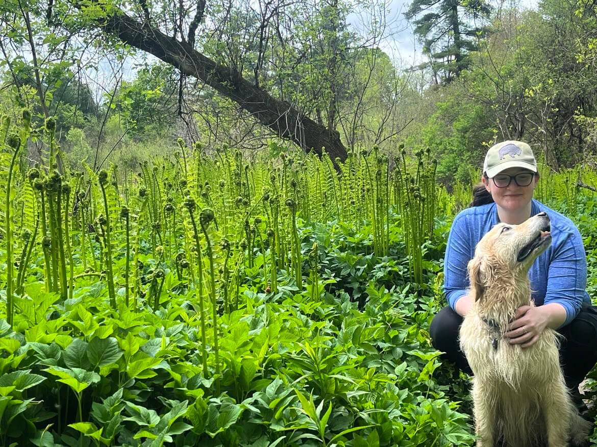 Noragh Devlin between two ferns with her dog