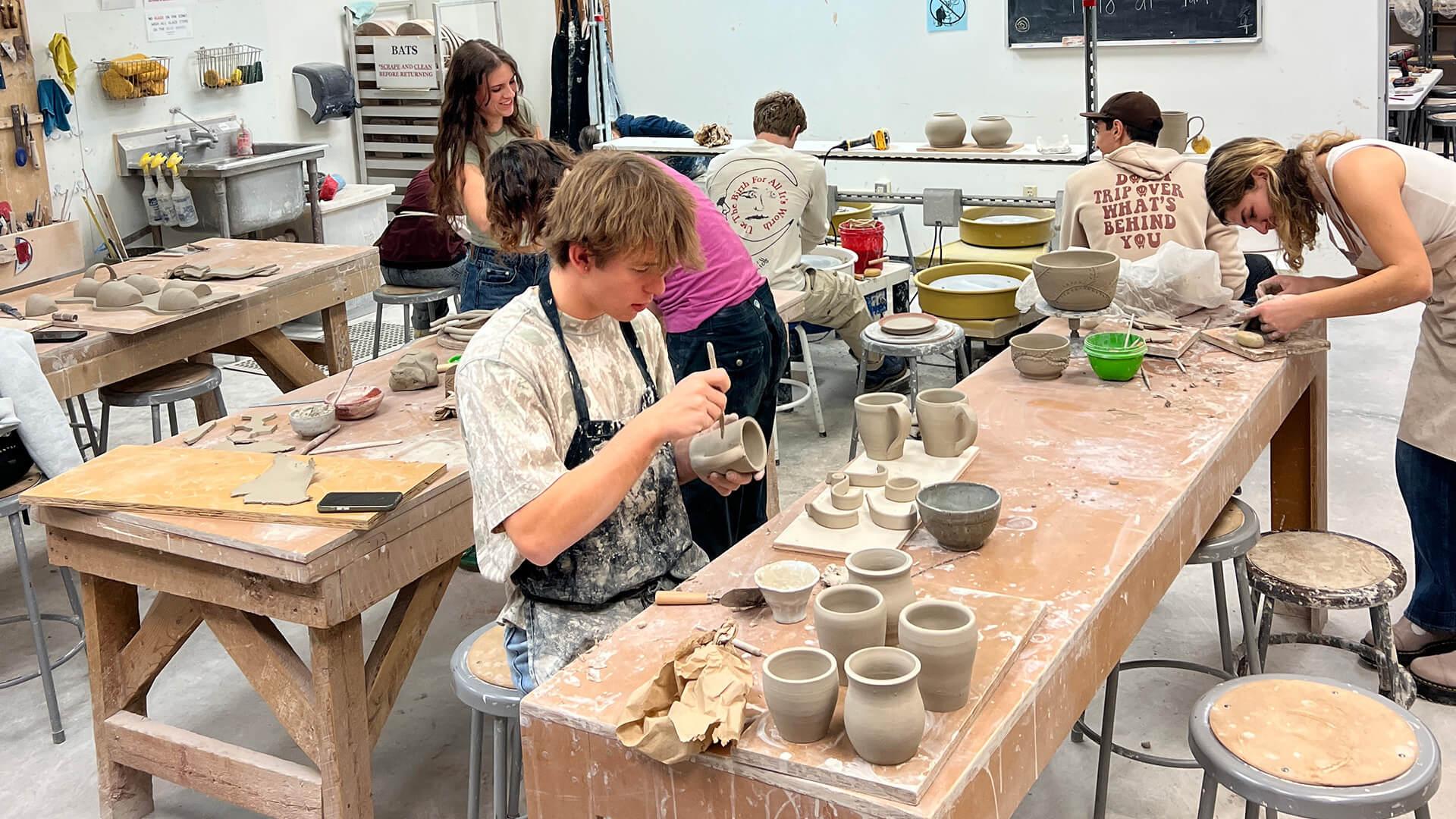 In a pottery studio, students collaborate on their projects, surrounded by tools and materials for creating ceramic art.