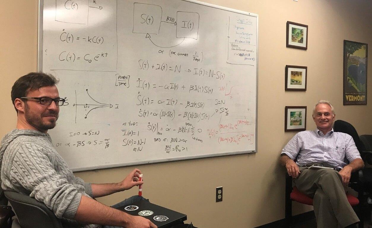 Lauent Hebert-Dufresne and Jason HT Bates sit on either side of a whiteboard covered in calculations