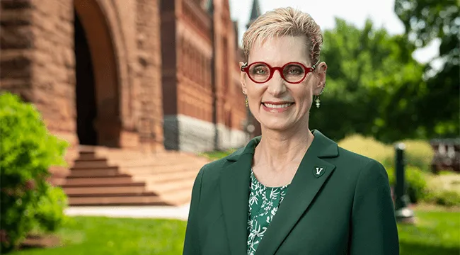 Marlene Tromp wears a green blazer and smiles on the UVM green