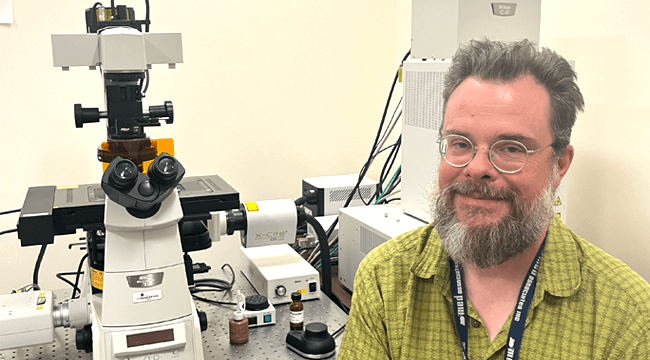 a man next to a complicated-looking microscope in a lab