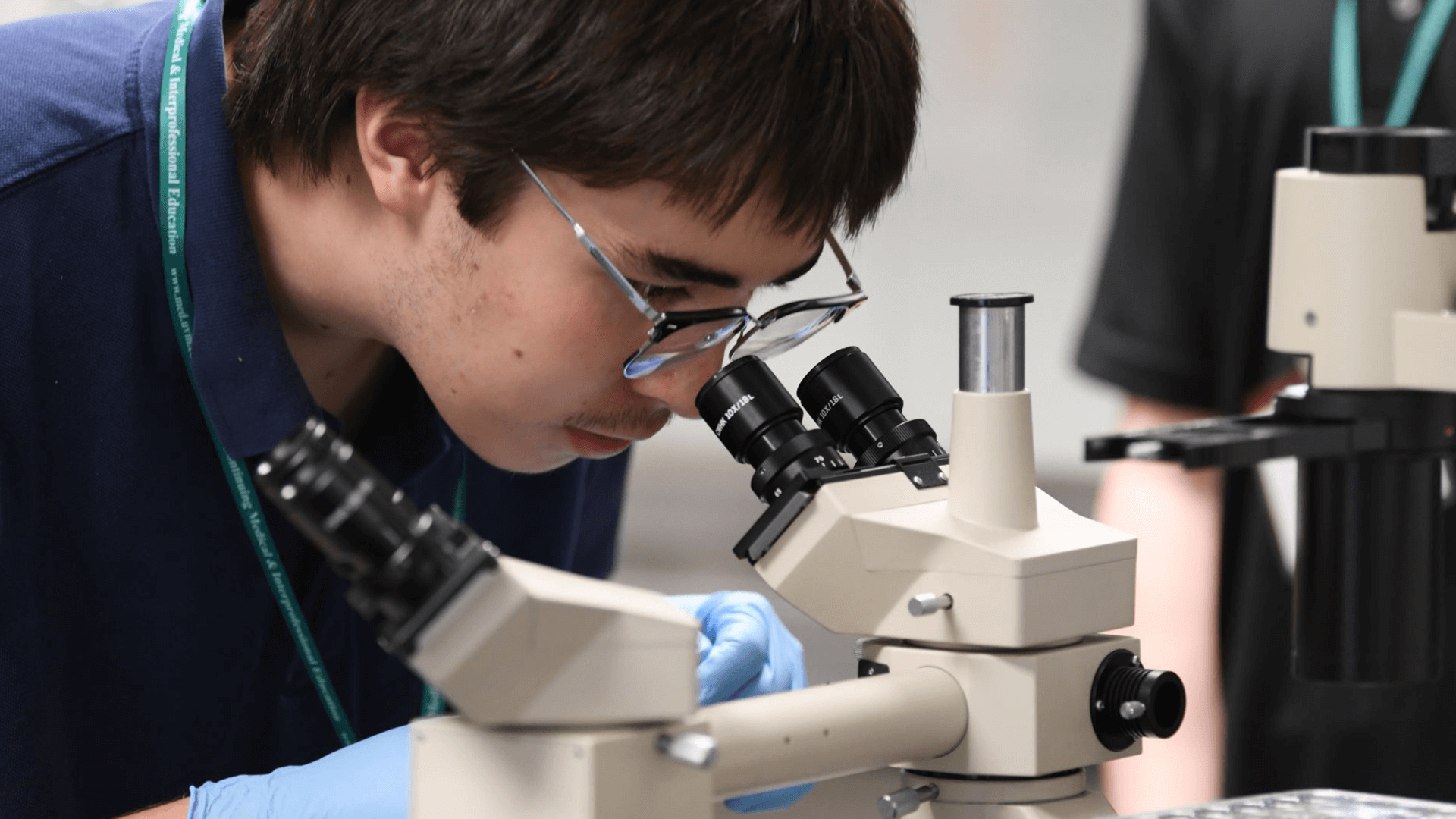 a high school student looking into a microscope in a lab