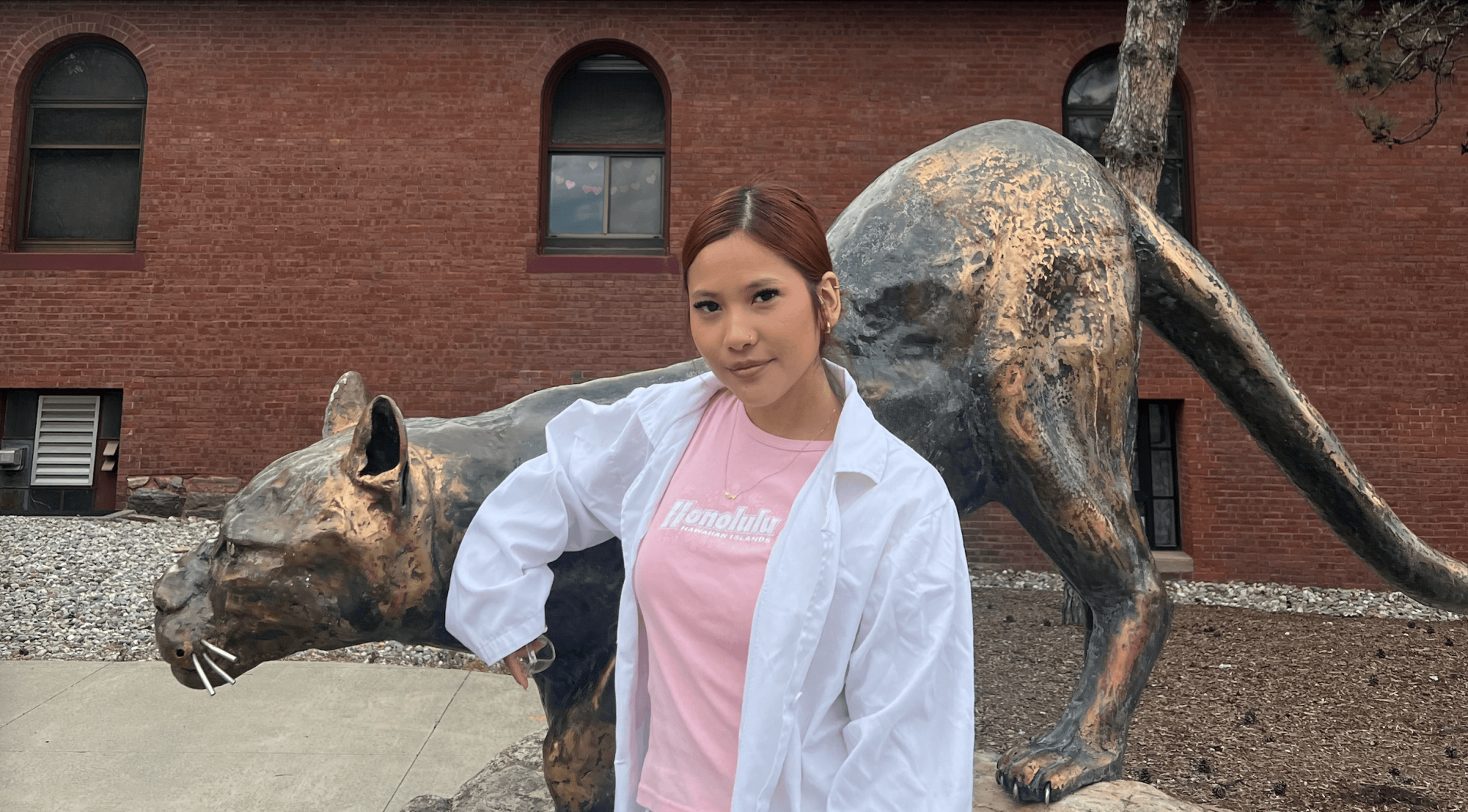 Student in a lab coat standing next to a statue of a catamount