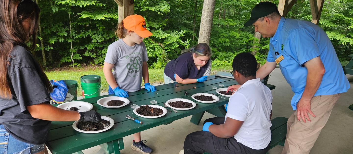campers with a teacher examining soil samples at a picnic table