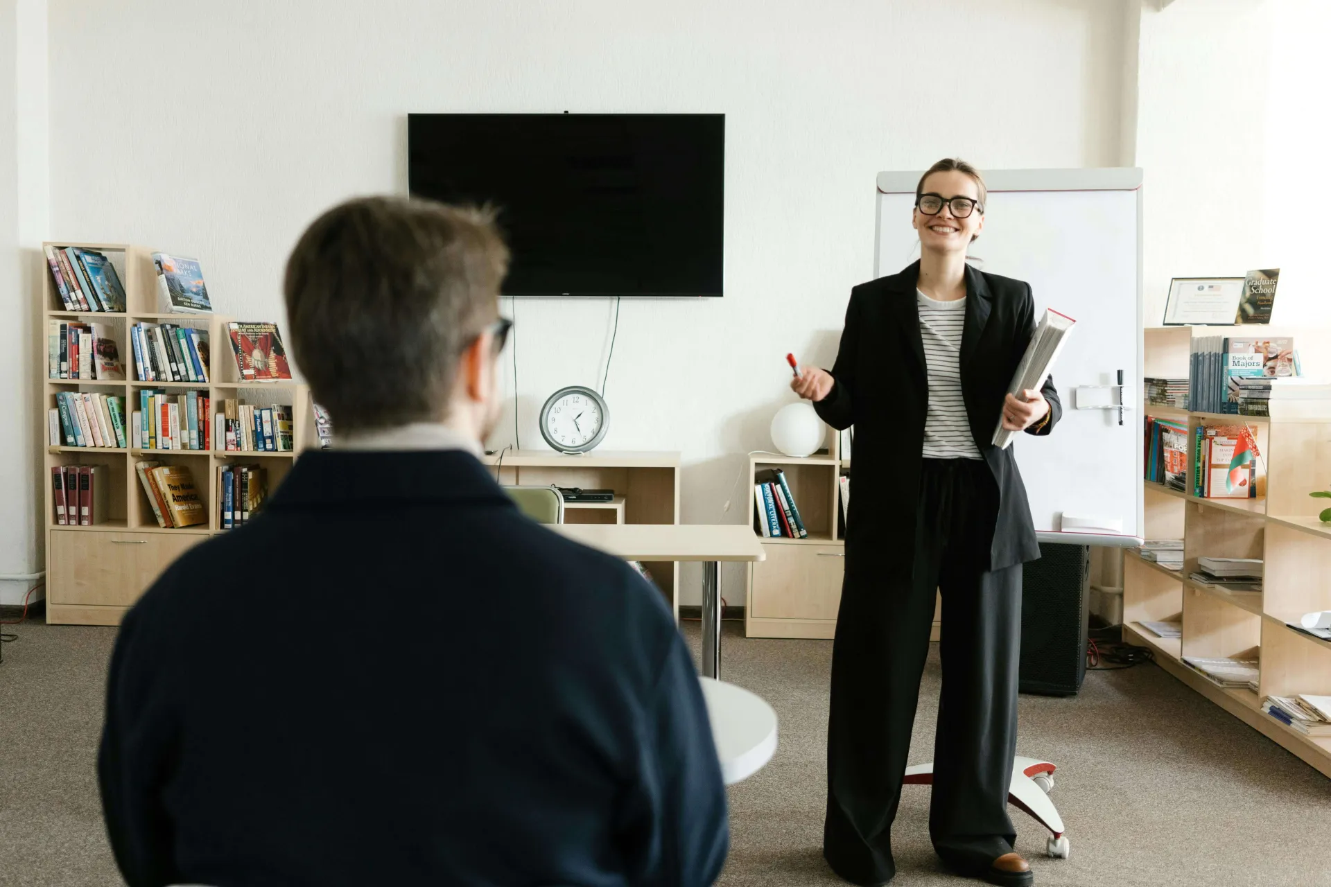 A white female faculty member grins while explaining something to a student in the front of the classroom