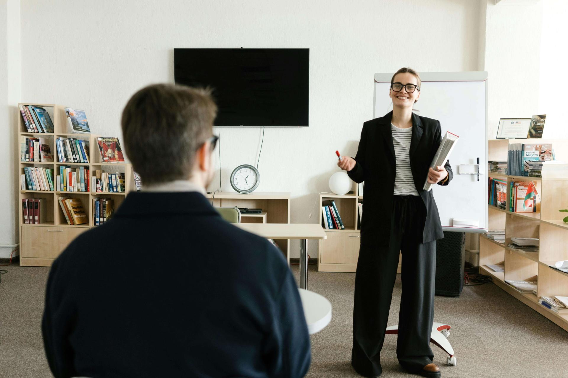 A white female faculty member grins while explaining something to a student in the front of the classroom