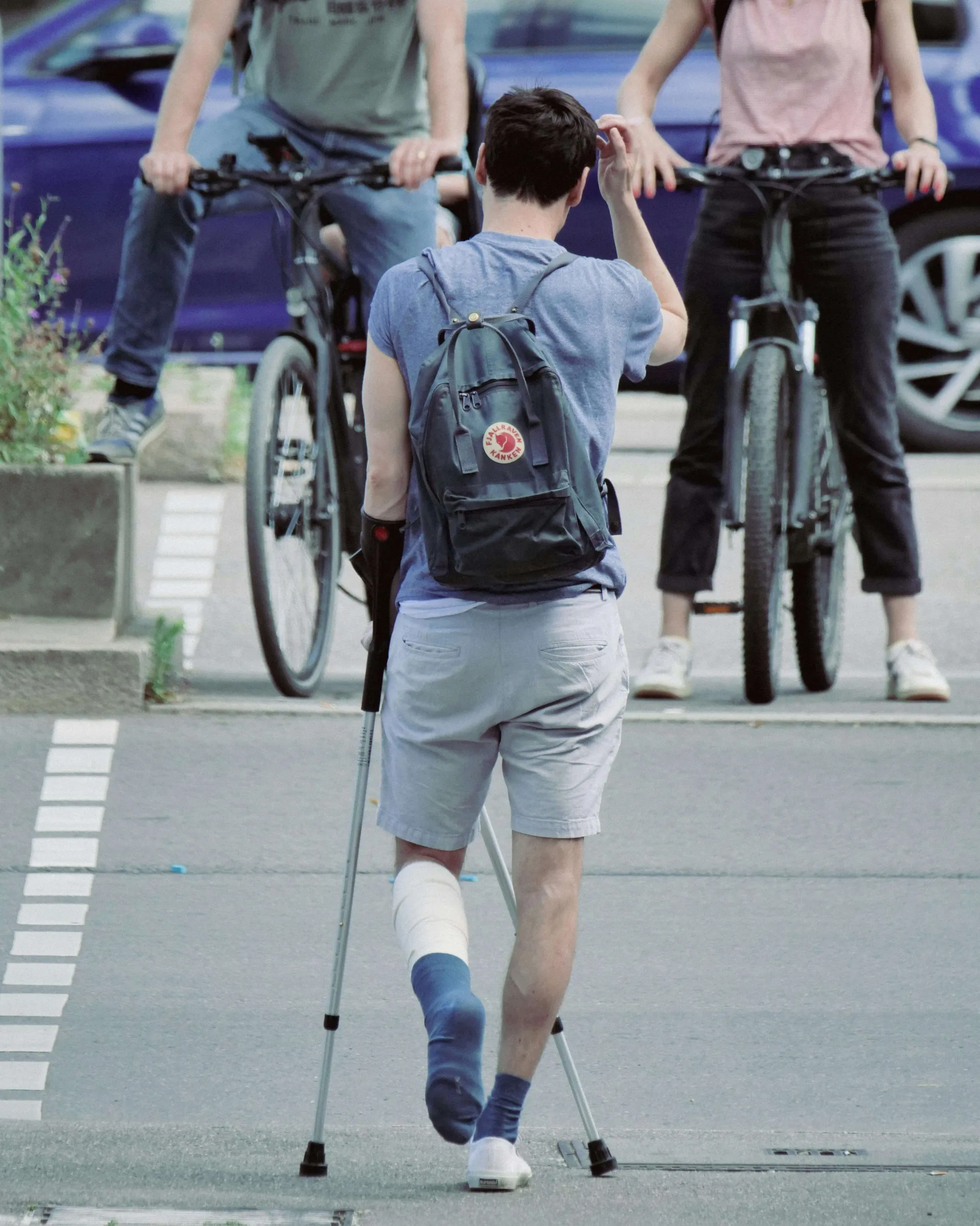 A college-aged student uses crutches to cross a parking lot