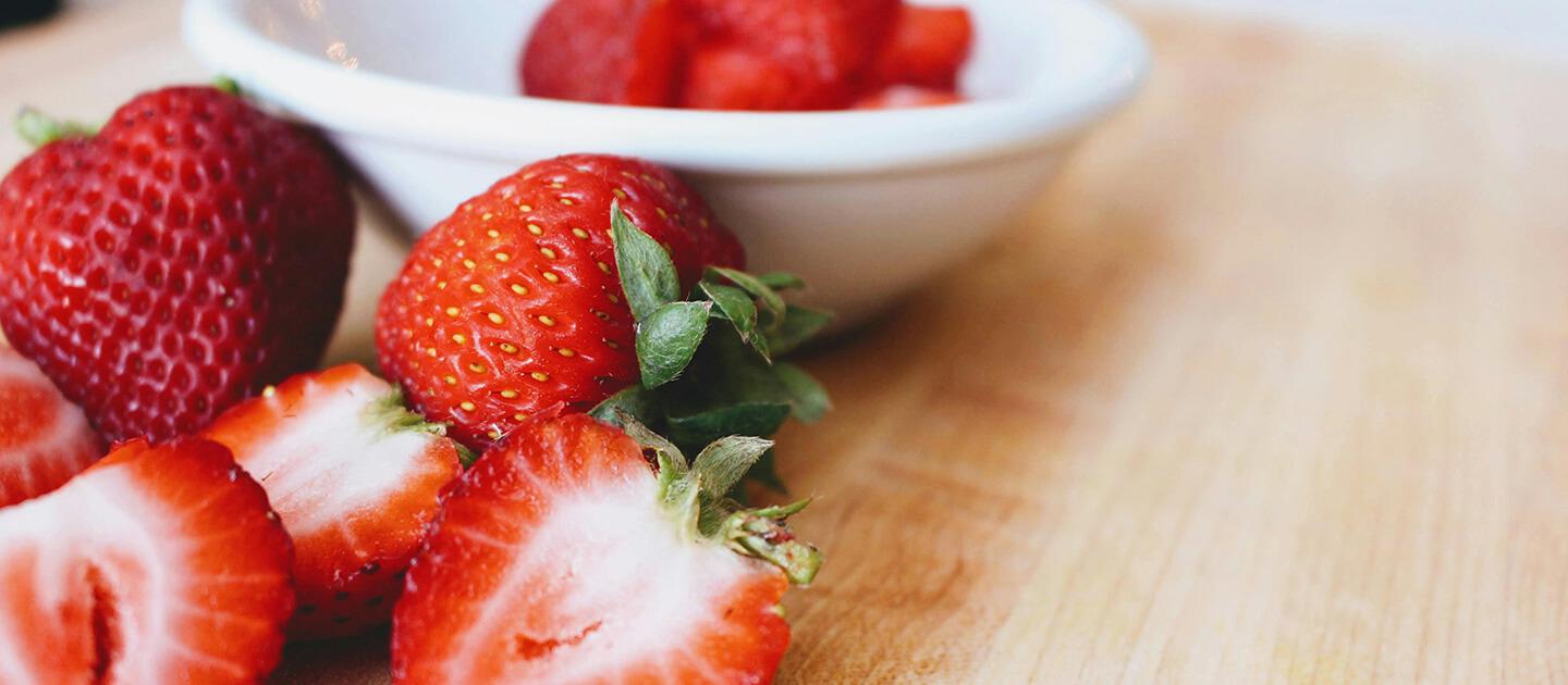 strawberries on a wooden table, some sliced, some in a bowl