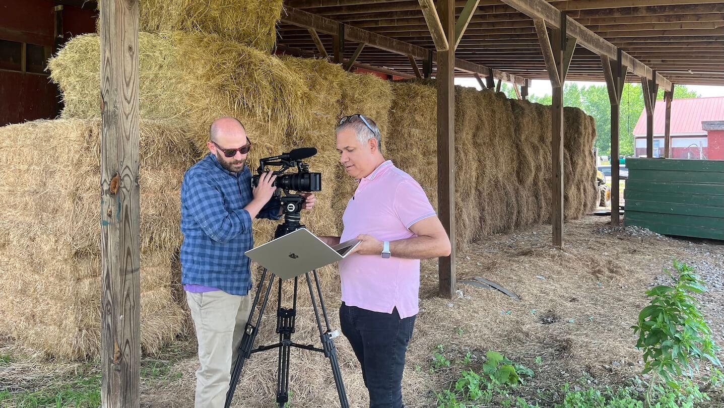 Two men stand by video camera inside a barn