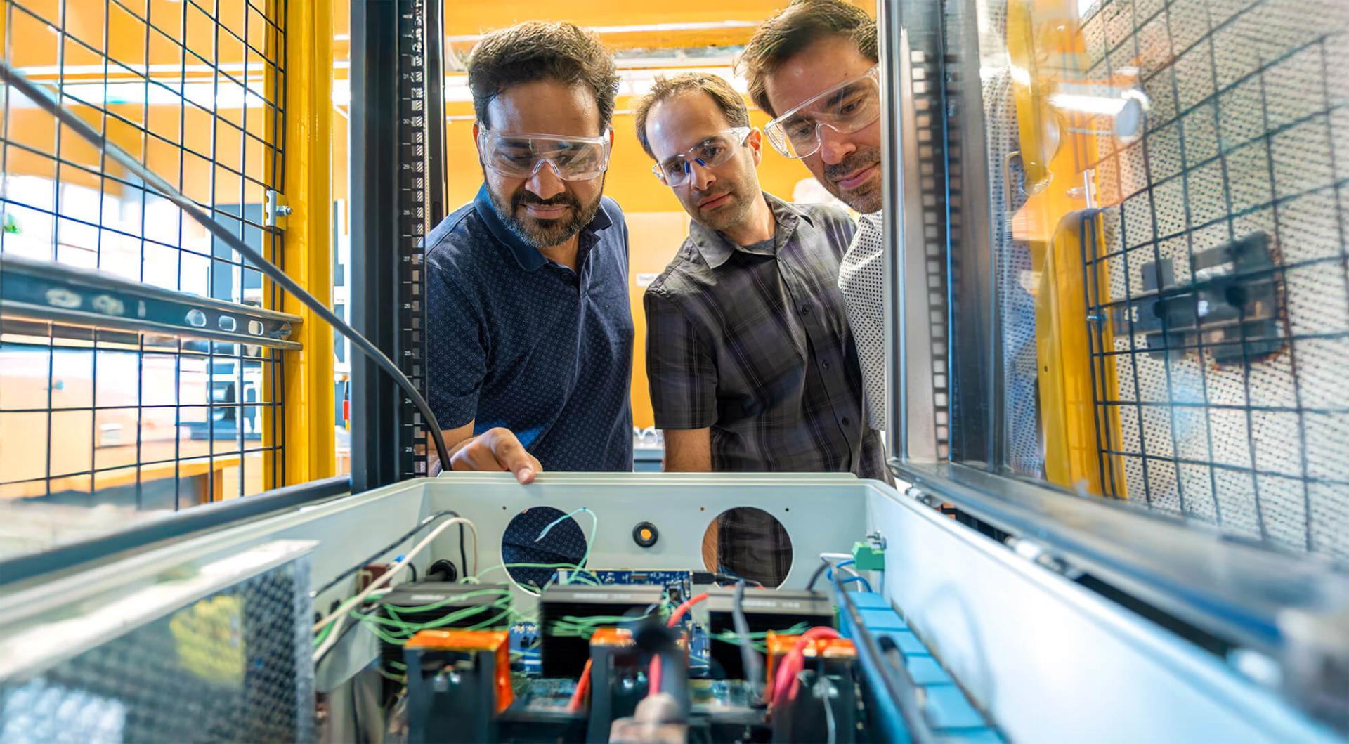Research Associate Tanmay Mishra, Associate Professor Hamid Ossareh, and Associate Professor Mads Almassalkhi examine new hardware in the Accelerated Testing Laboratory.