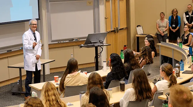 man in a white coat addressing a group of new medical students