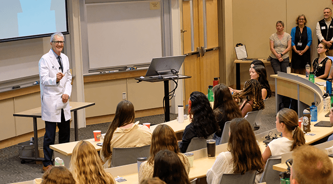 man in a white coat addressing a group of new medical students