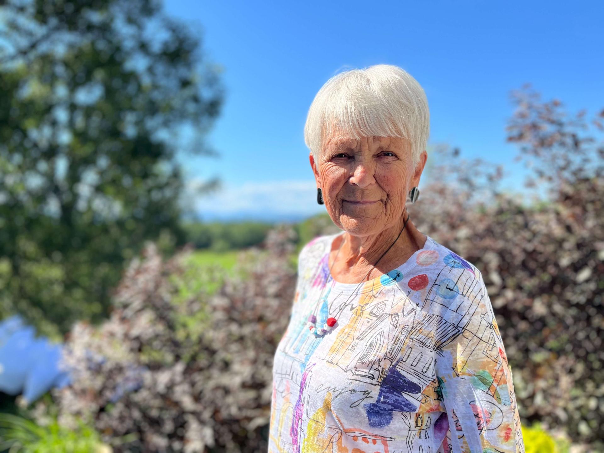 woman with a colorful shirt standing in a garden on a bright sunny day with a blue sky 