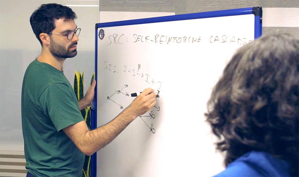 Giulio Burgio and Juniper Lovato discuss their research at a whiteboard