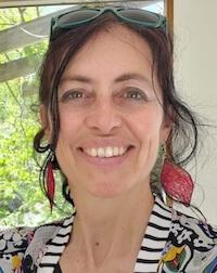 A woman with dark hair pulled back and red earrings smiles.
