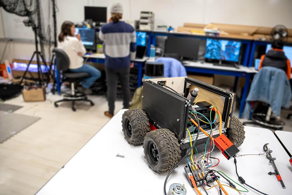 A wheeled robot sits in the foreground of an electrical engineering lab