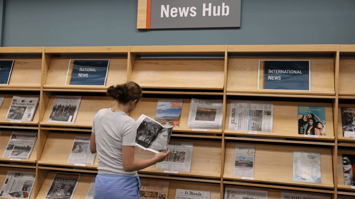 Student looking at a newspaper in the Howe news hub
