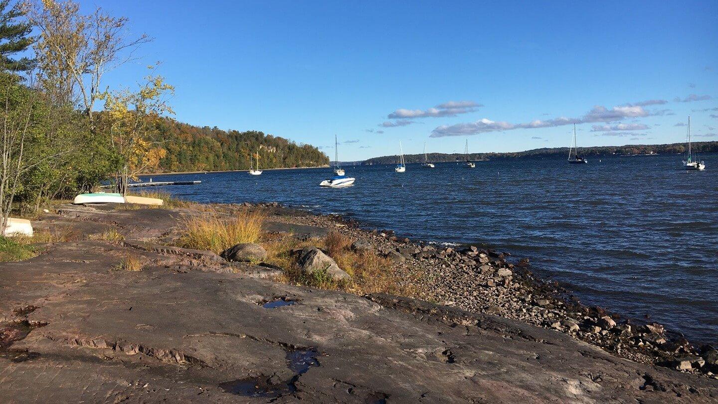 a rocky shoreline with a lake, boats and blue sky in the background