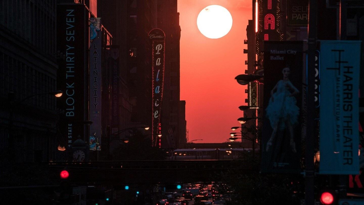 a sun sets in an orange sky over a city street