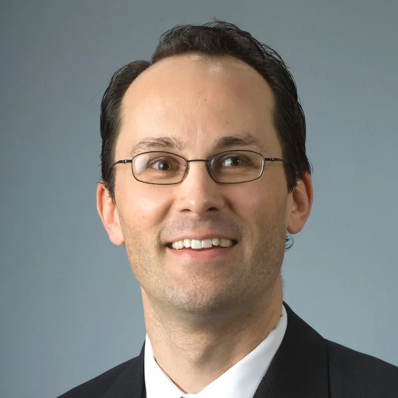 headshot of a smiling man wearing glasses