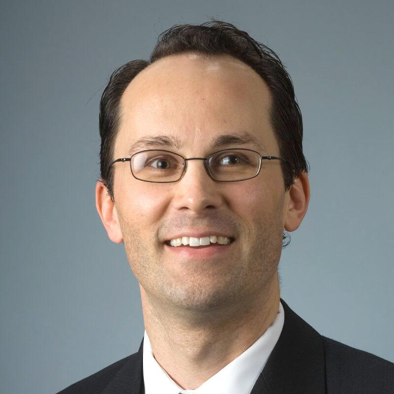 headshot of a smiling man wearing glasses