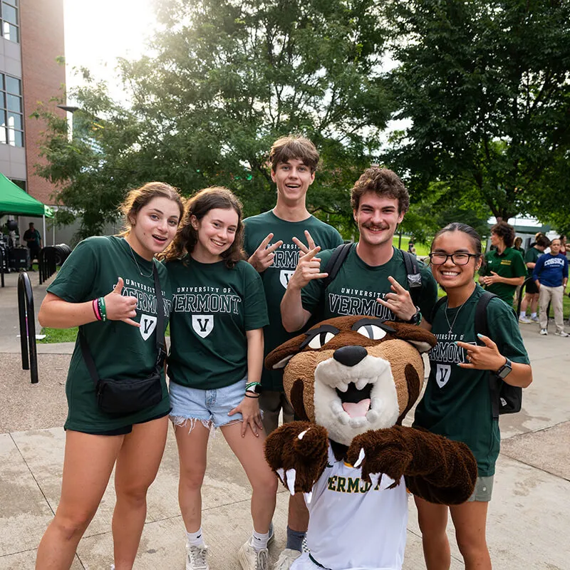 Group of students in green shirts gather around Rally Cat smiling. 