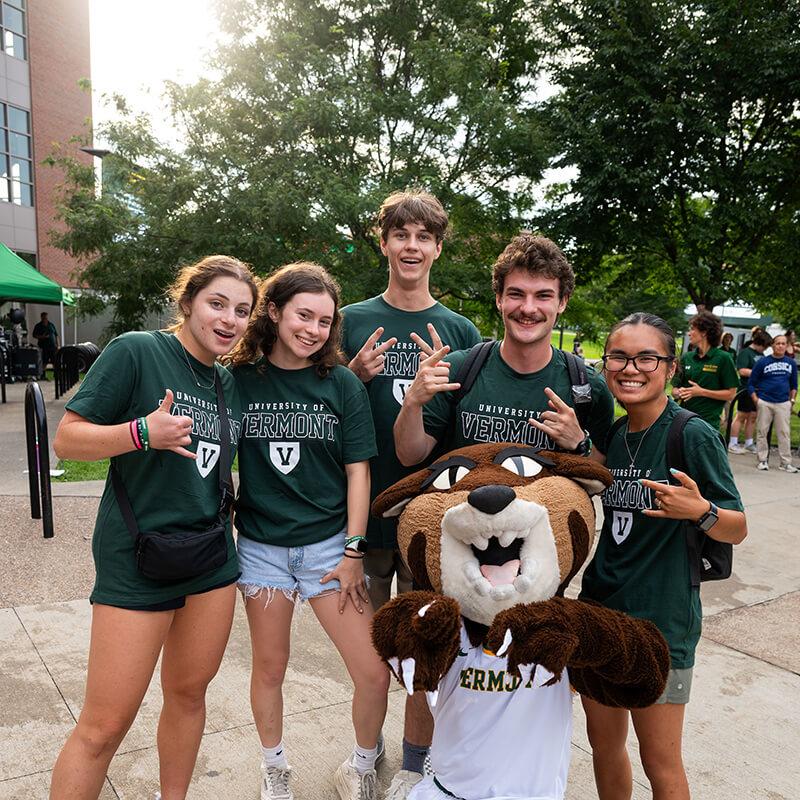 Group of students in green shirts gather around Rally Cat smiling. 