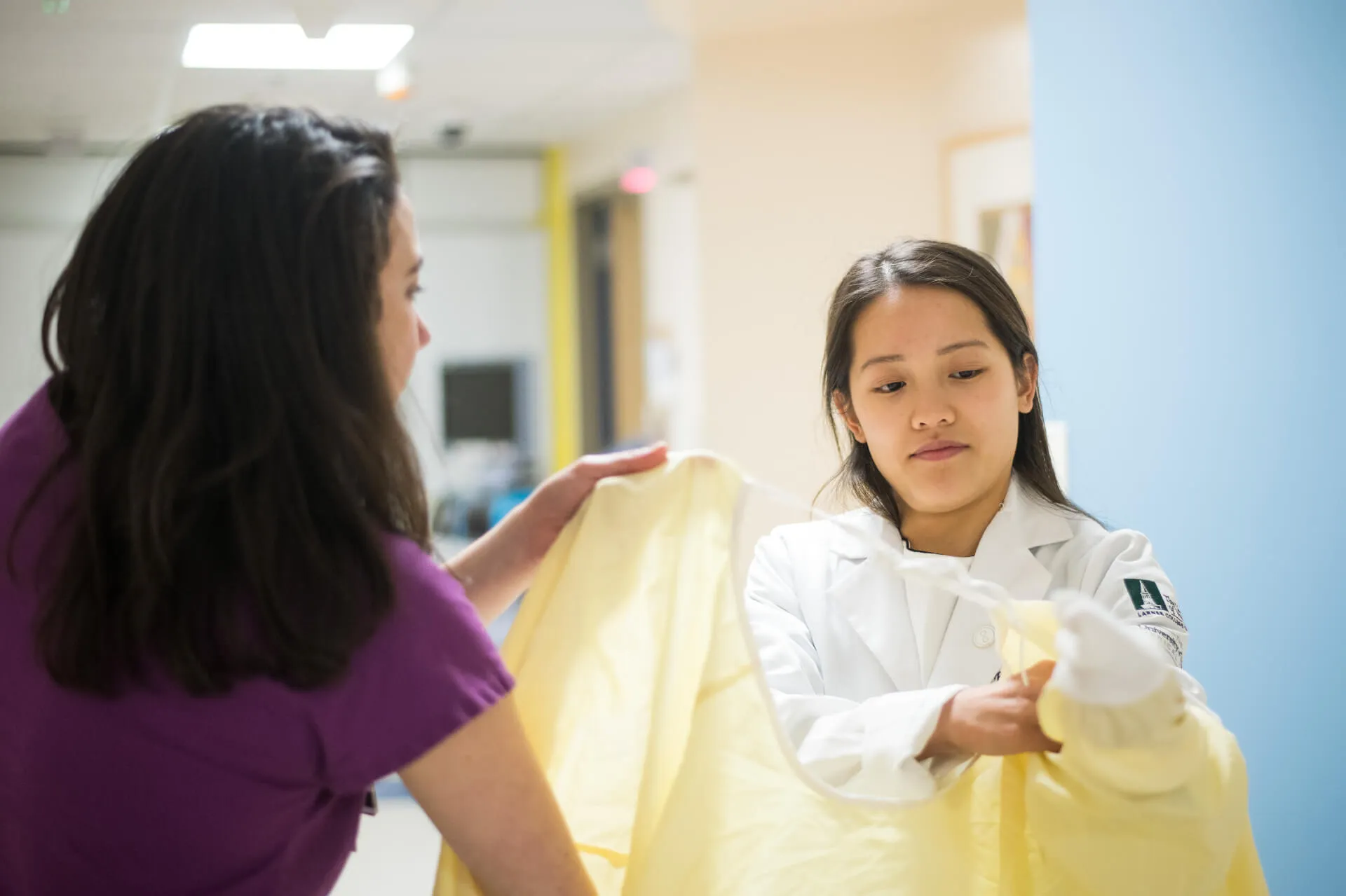 young person trying on sterile gown with a nurse helping