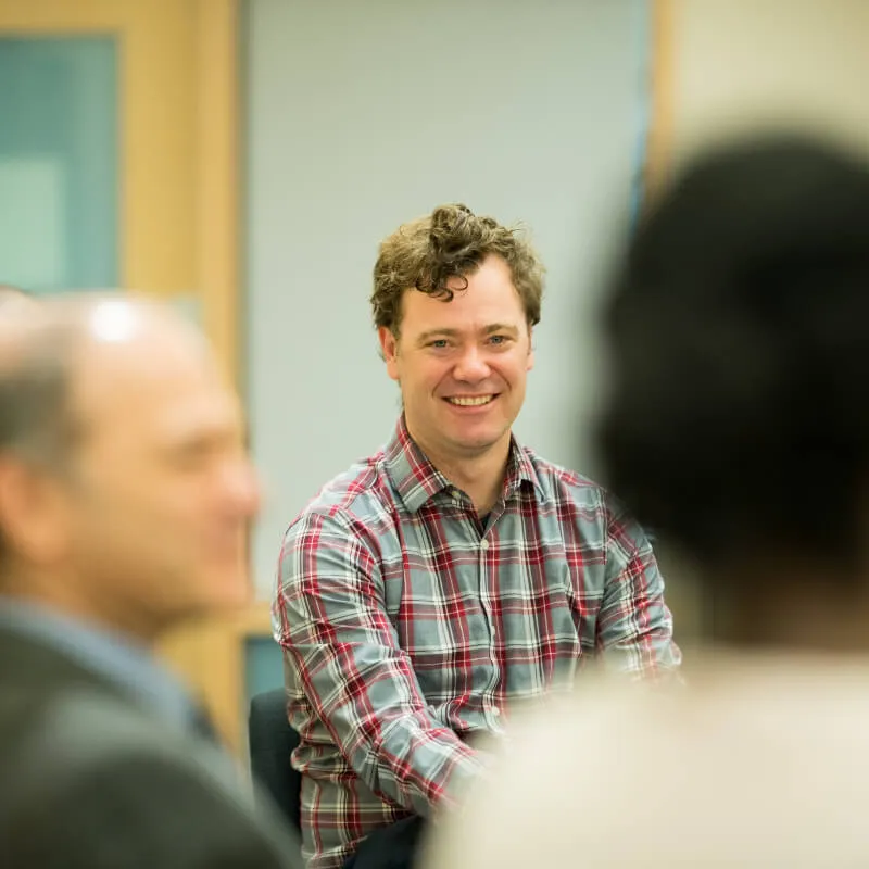 man smiling as two other people sit nearby