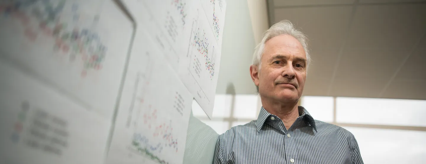 Man leaning on a whiteboard with research notation on it