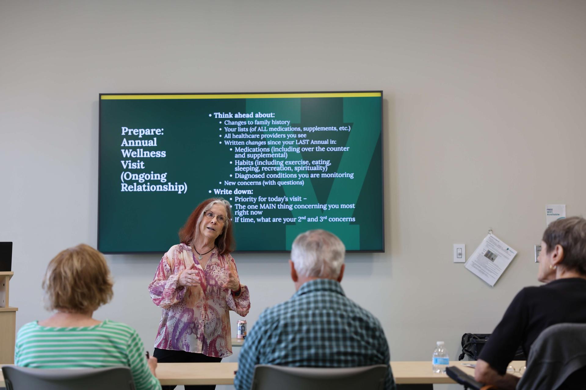 Geri Amori speaks in front of a projector screen to an audience.