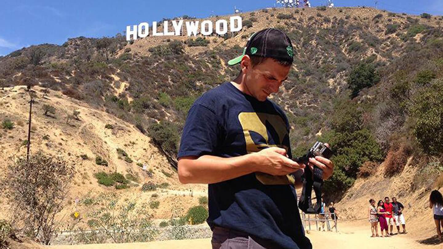 Person holding a camera/phone near the Hollywood sign on a sunny day.
